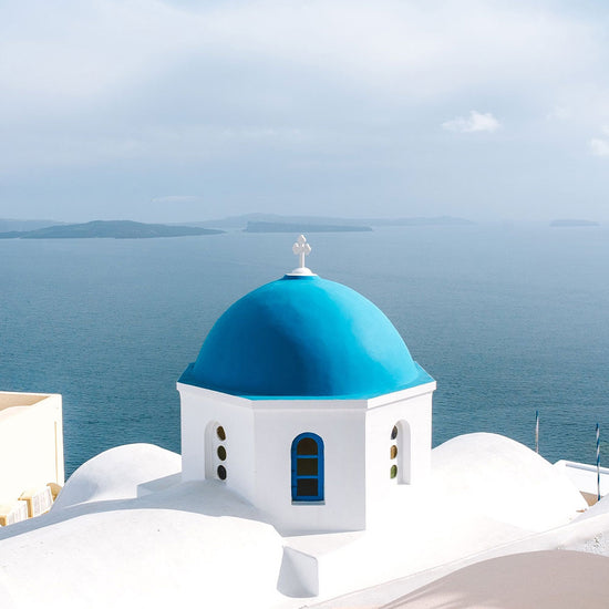 Blue-domed church with white walls overlooking the ocean in Santorini, Greece.