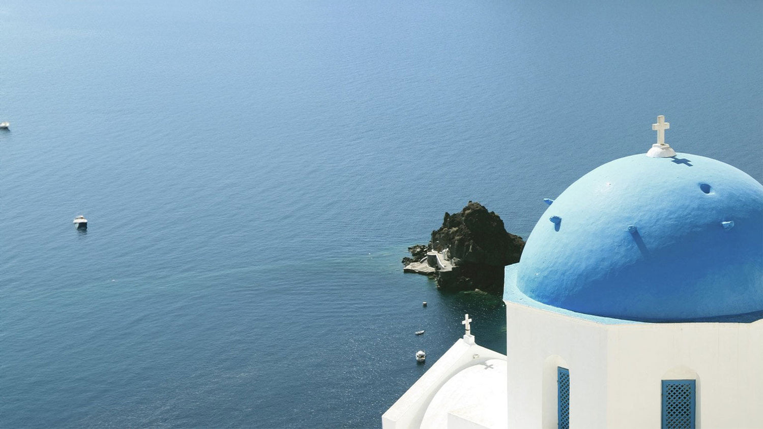 Blue-domed church by the sea with clear blue sky