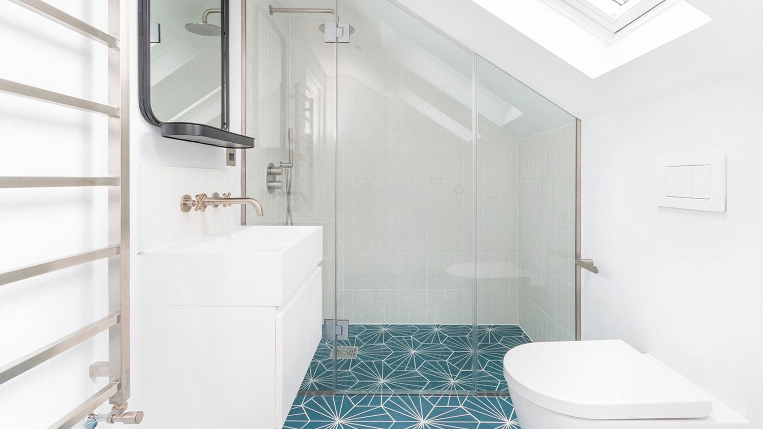 Modern bathroom with glass shower enclosure, white tiles, and blue geometric patterned floor.