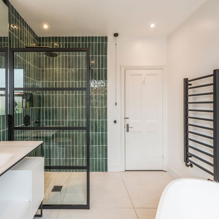 Modern bathroom with glass shower enclosure, green tiles, and white door.