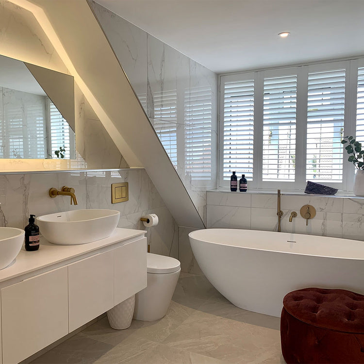 Modern bathroom with white fixtures, a bathtub, and a window with blinds.