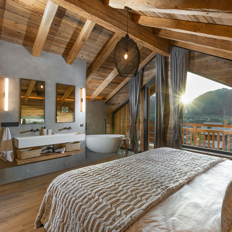 Modern bedroom with wooden beams, a bed, and a bathroom in the background.