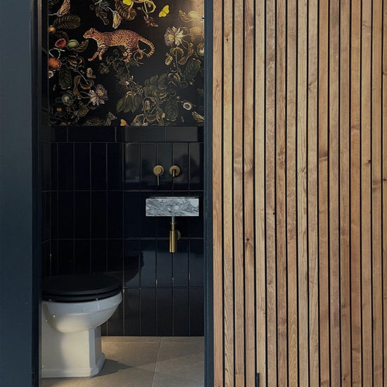 Bathroom with black tiled wall, white toilet, and wooden slat wall.