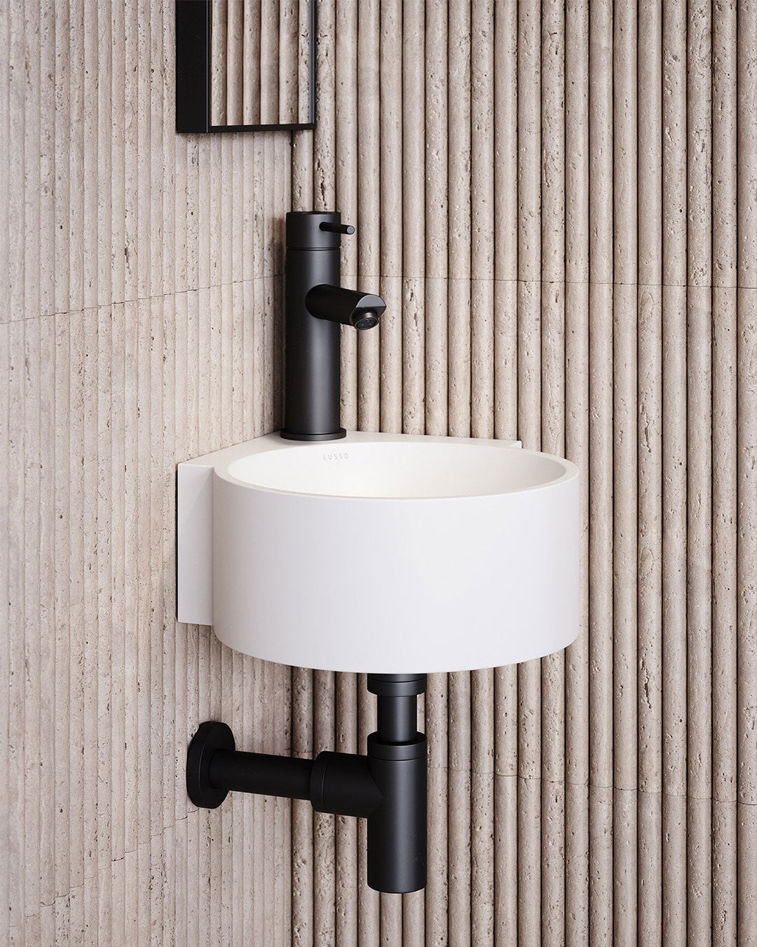 White wall-mounted sink with black faucet against a textured beige wall.