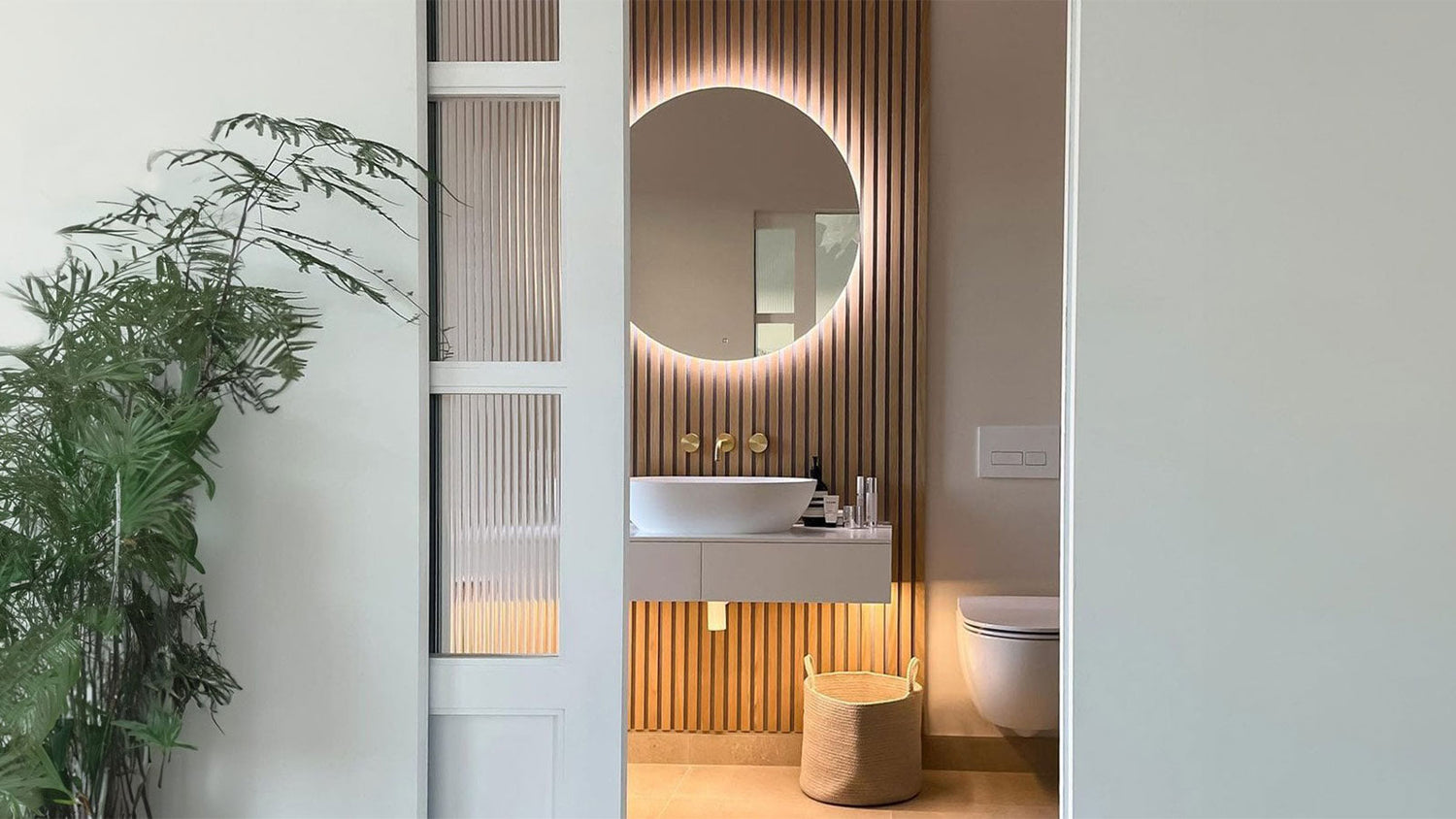Modern bathroom with a sink, mirror, and toilet, featuring a plant on the left.