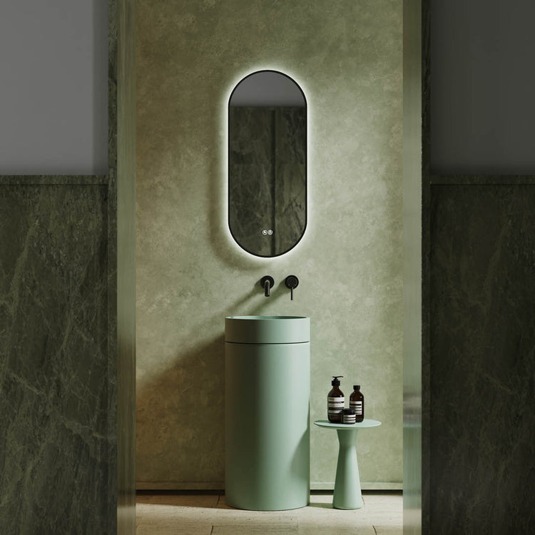Green cylindrical sink with mirror and bottles in a bathroom setting