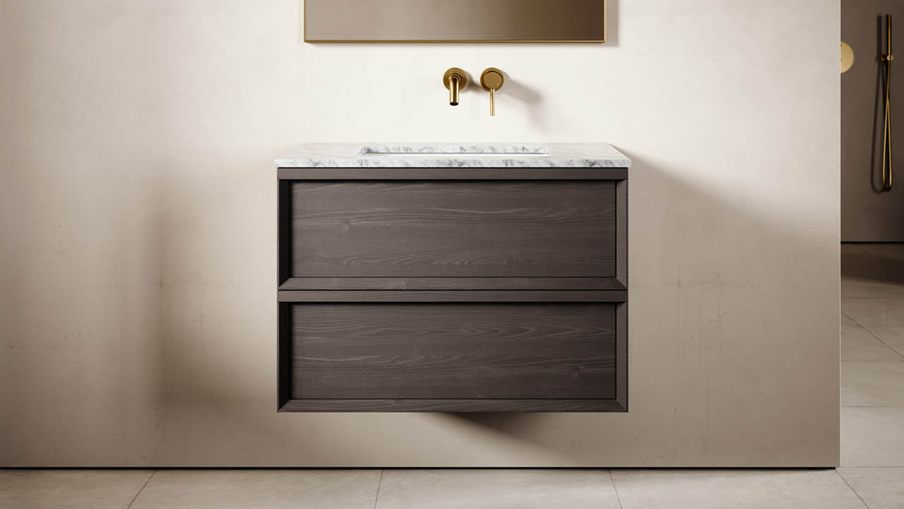 Bathroom vanity with marble countertop and gold faucet against a beige wall.