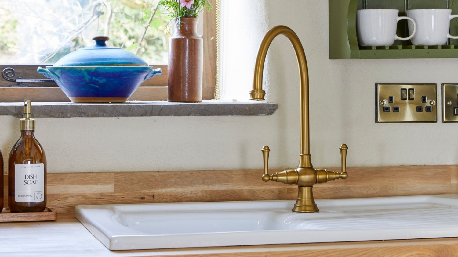 Kitchen sink with gold faucet, wooden countertop, and window in background