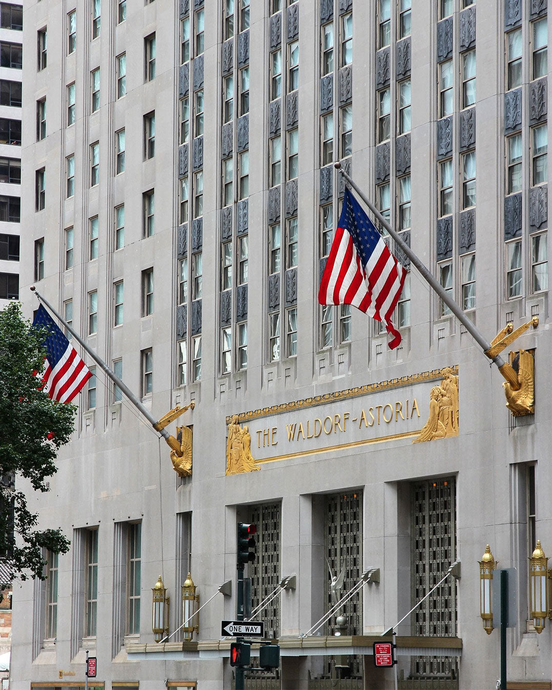 Facade of The Waldorf-Astoria hotel with American flags and gold accents.