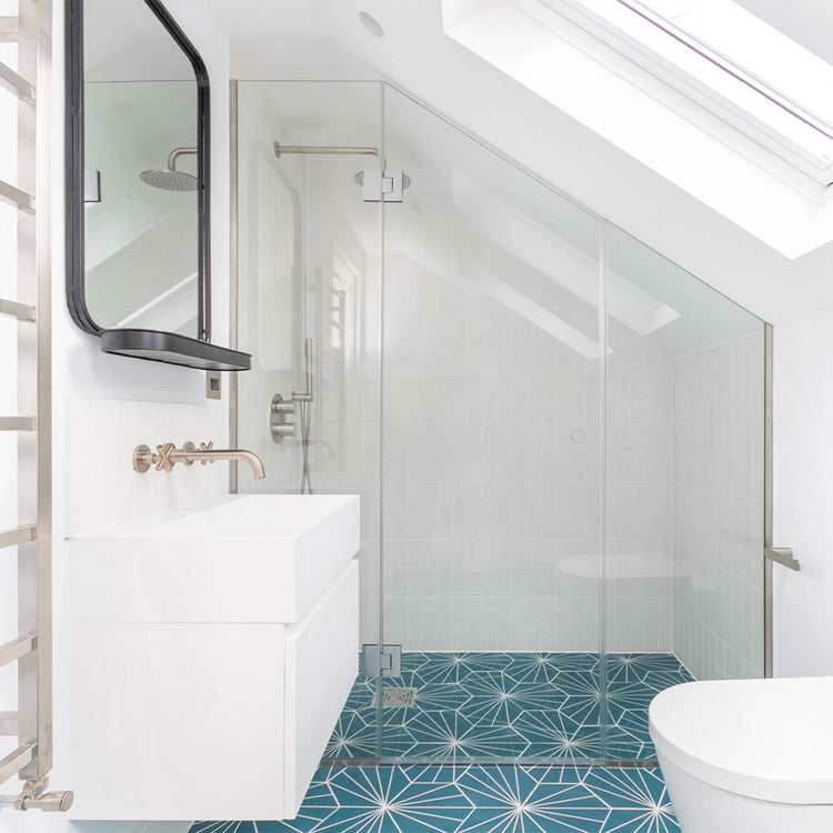 Modern bathroom with glass shower enclosure, white sink, and blue patterned tiles on the floor.