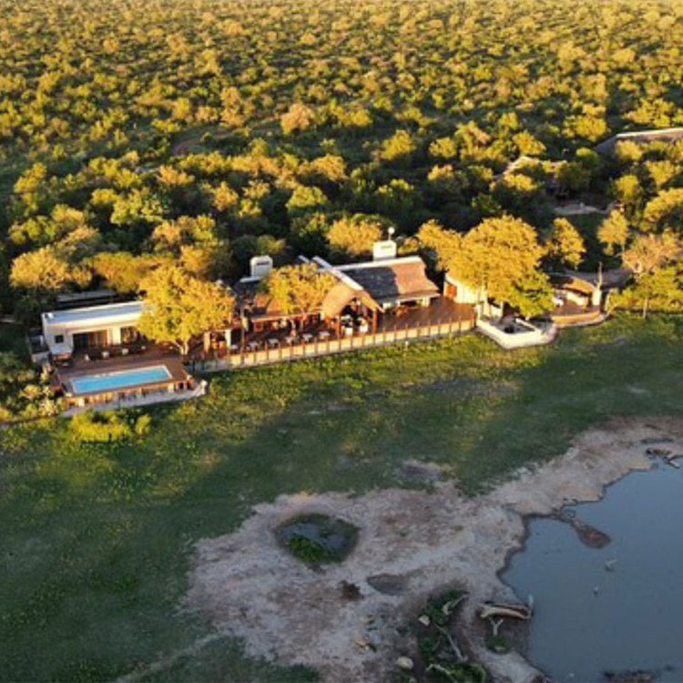 Aerial view of a lodge surrounded by lush greenery and a water body.