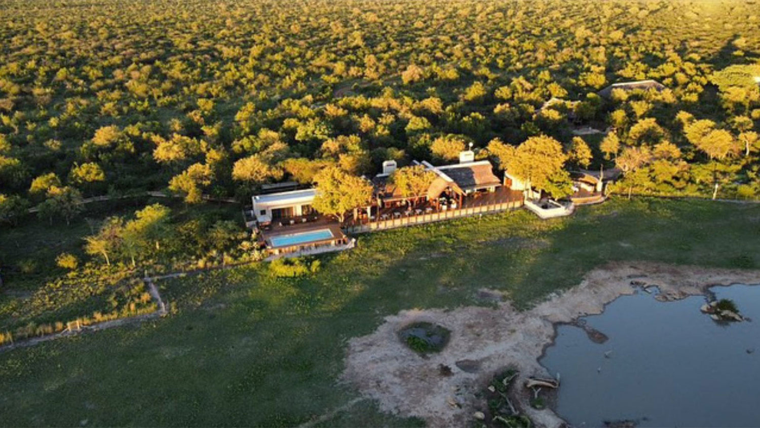 Aerial view of a lodge surrounded by dense greenery and a water body.