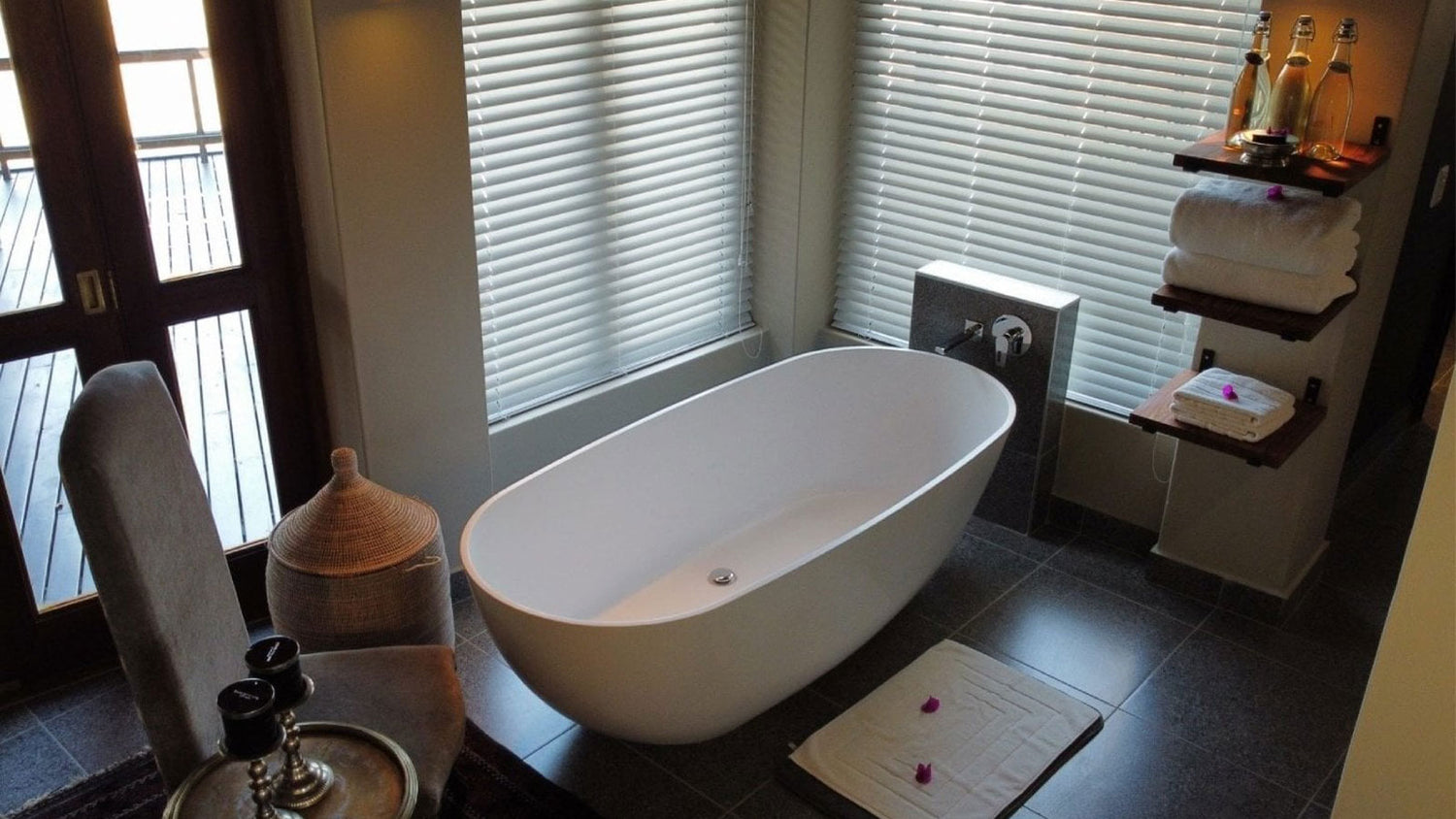 Modern bathroom with a freestanding bathtub, towels, and a shelf with bottles.
