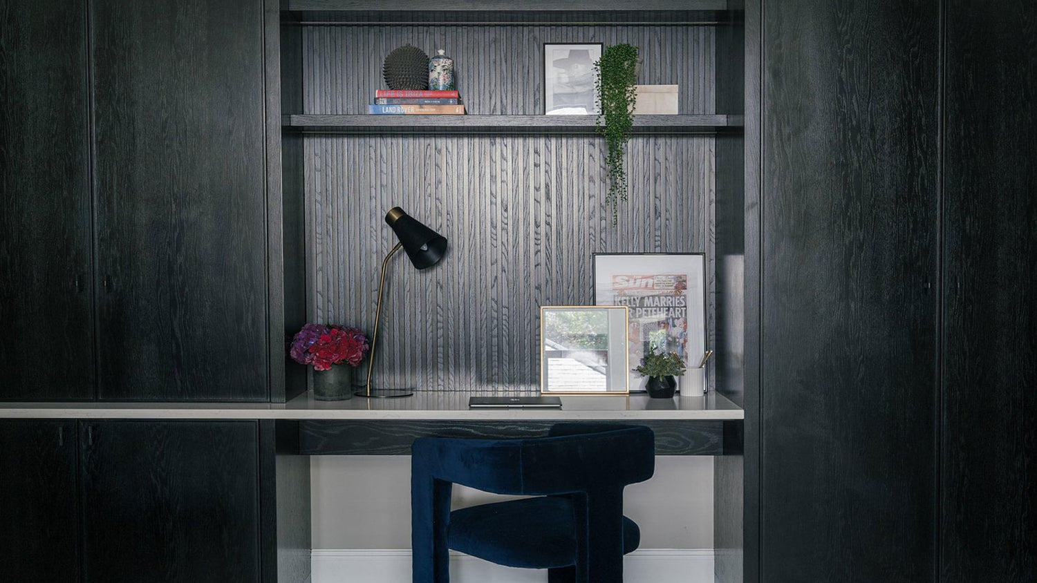 Modern home office with a desk, chair, and decorative items against a dark wall.