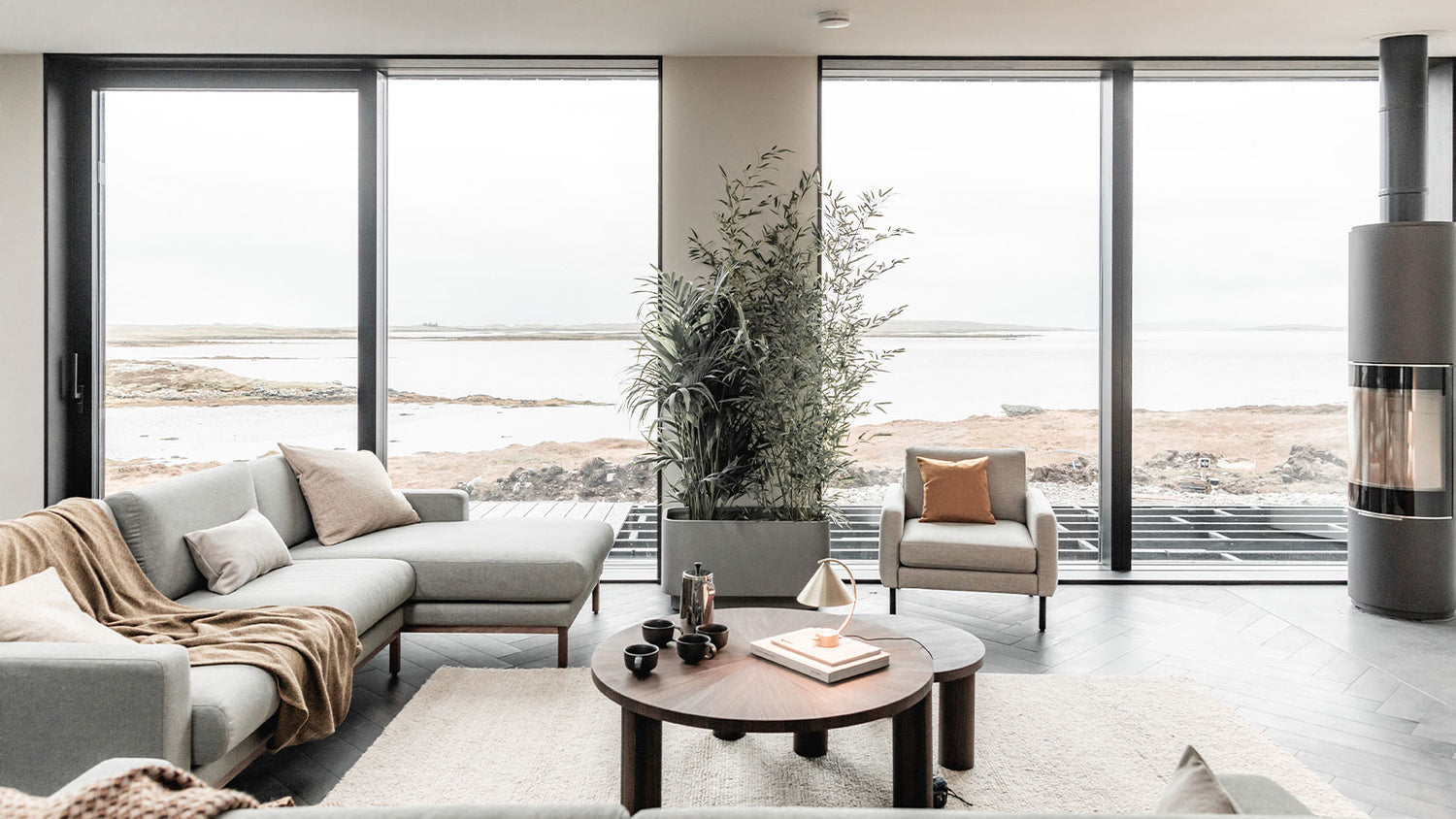 Modern living room with large windows, gray sectional sofa, and wooden coffee table.