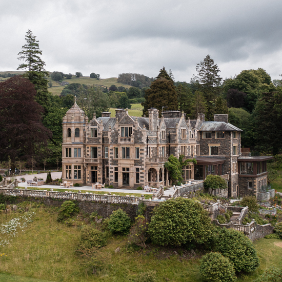 Large stone mansion surrounded by greenery on a cloudy day