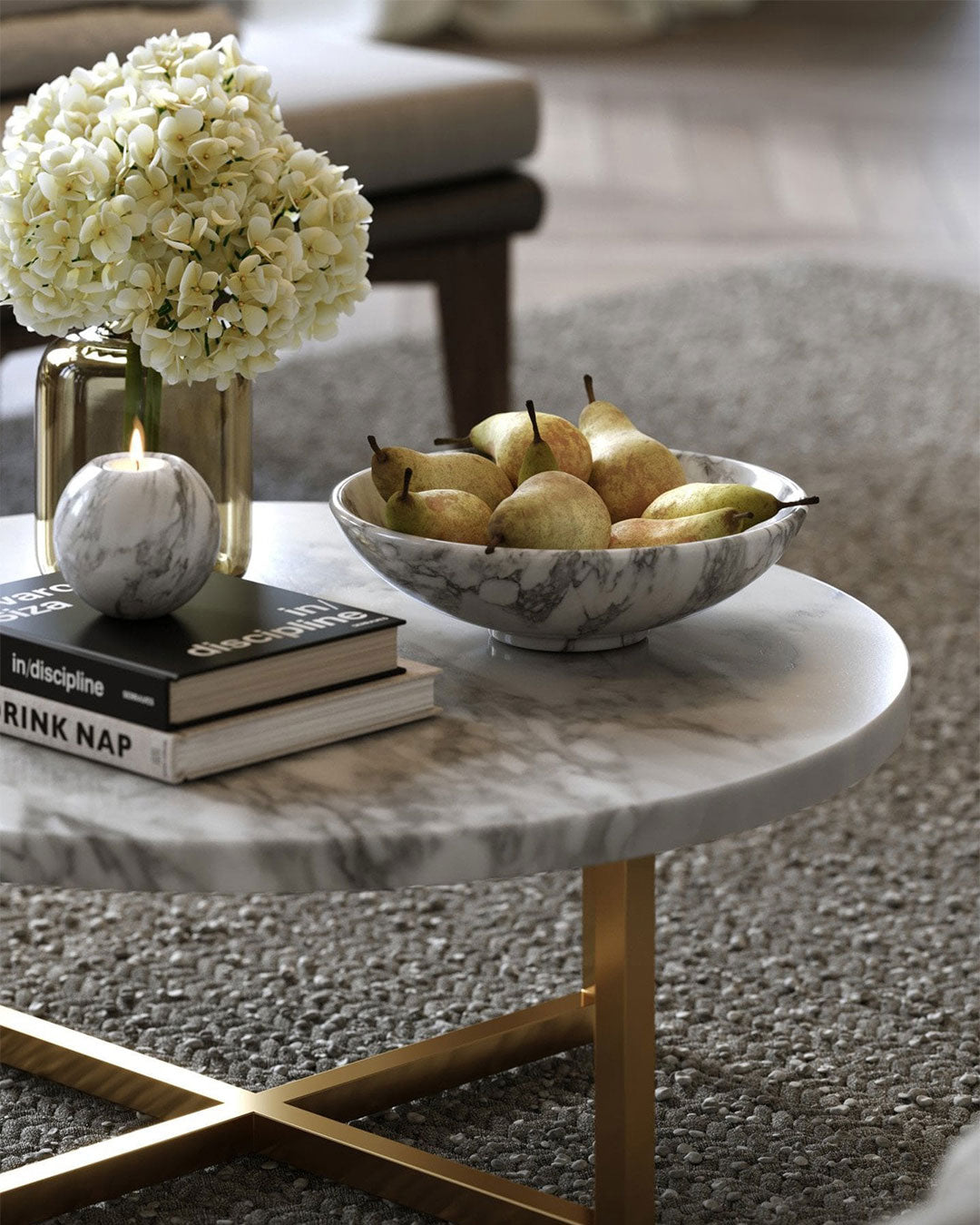 Marble coffee table with books, a candle, and a bowl of pears in a living room setting.