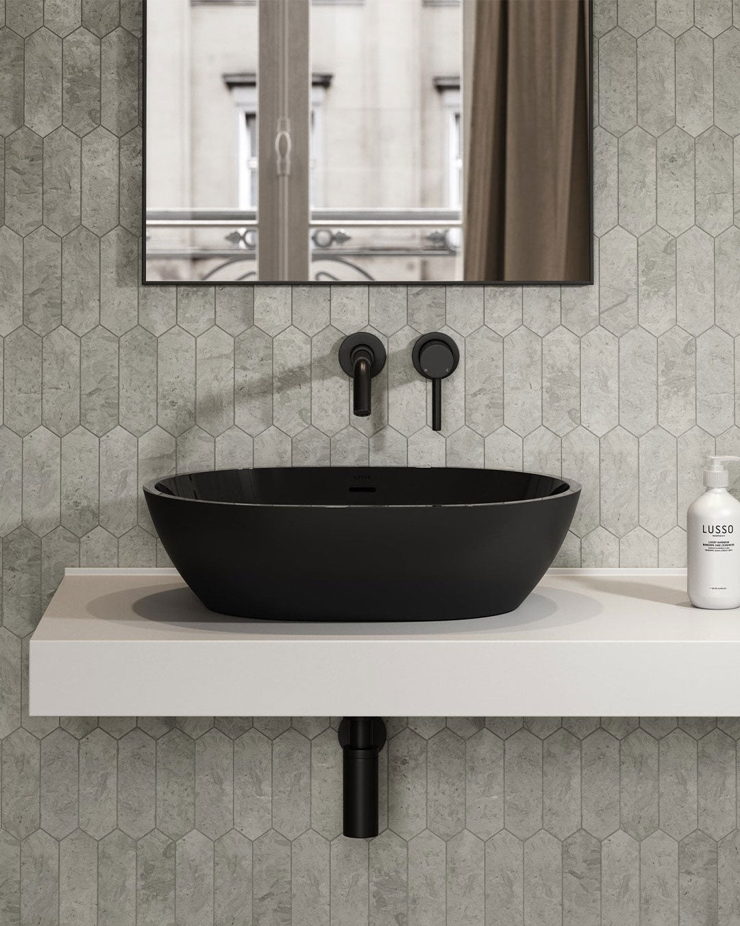 Black sink on a white countertop with hexagonal grey tiles and a mirror above.