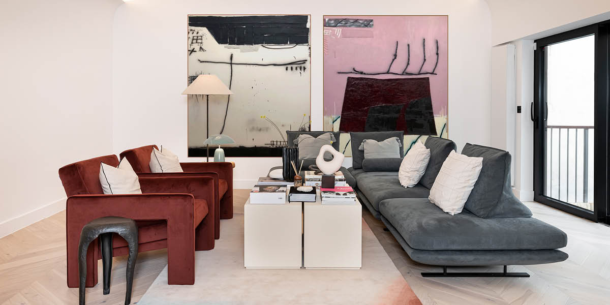 Modern living room with a grey sofa, red chairs, and abstract art on the wall.