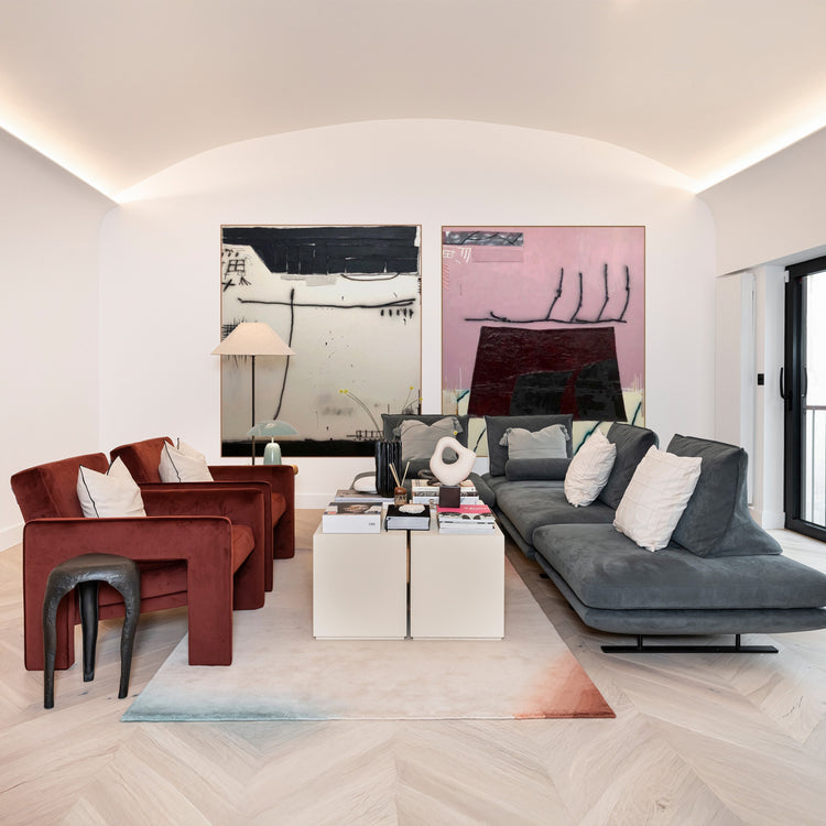 Modern living room with grey sofa, red chairs, and abstract art on the wall.