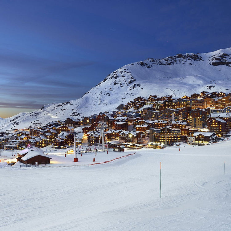 Snowy mountain village at night with illuminated buildings and ski lifts.