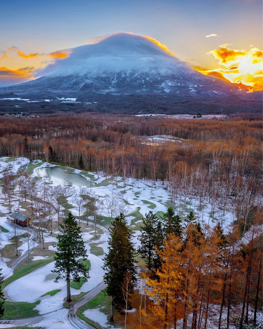 Snowy landscape with a mountain in the background during sunset.