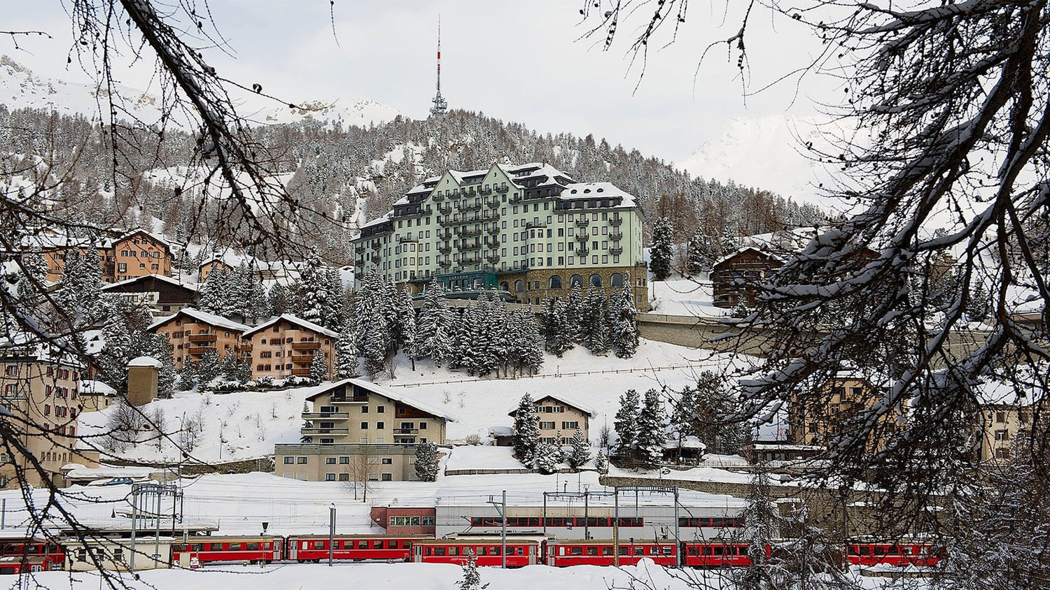Snow-covered mountain village with a red train and buildings in the background