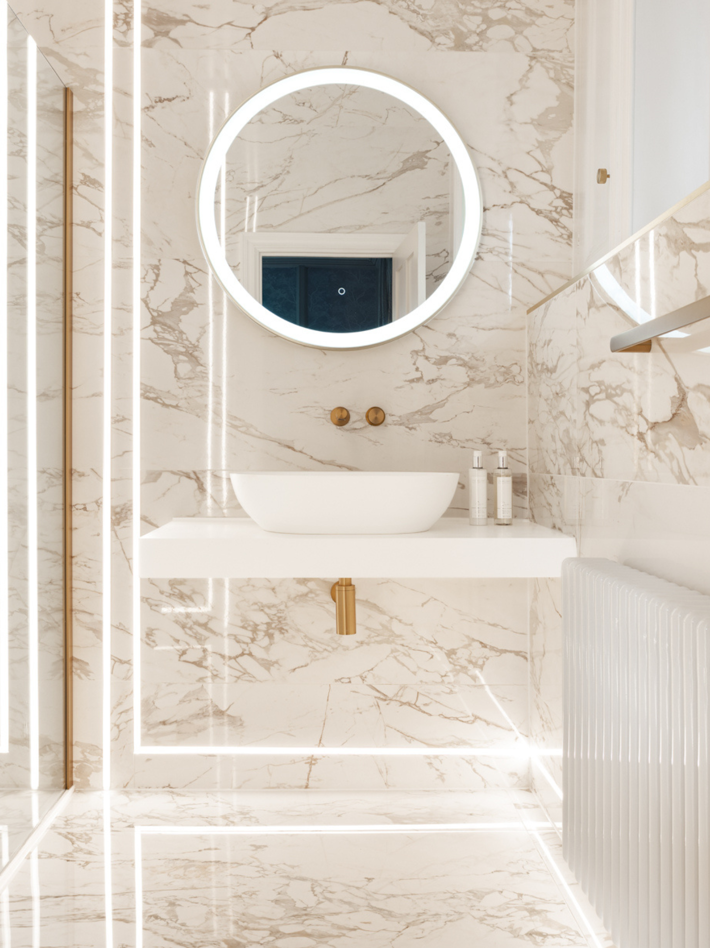 Bathroom with marble walls, round mirror, and white sink.