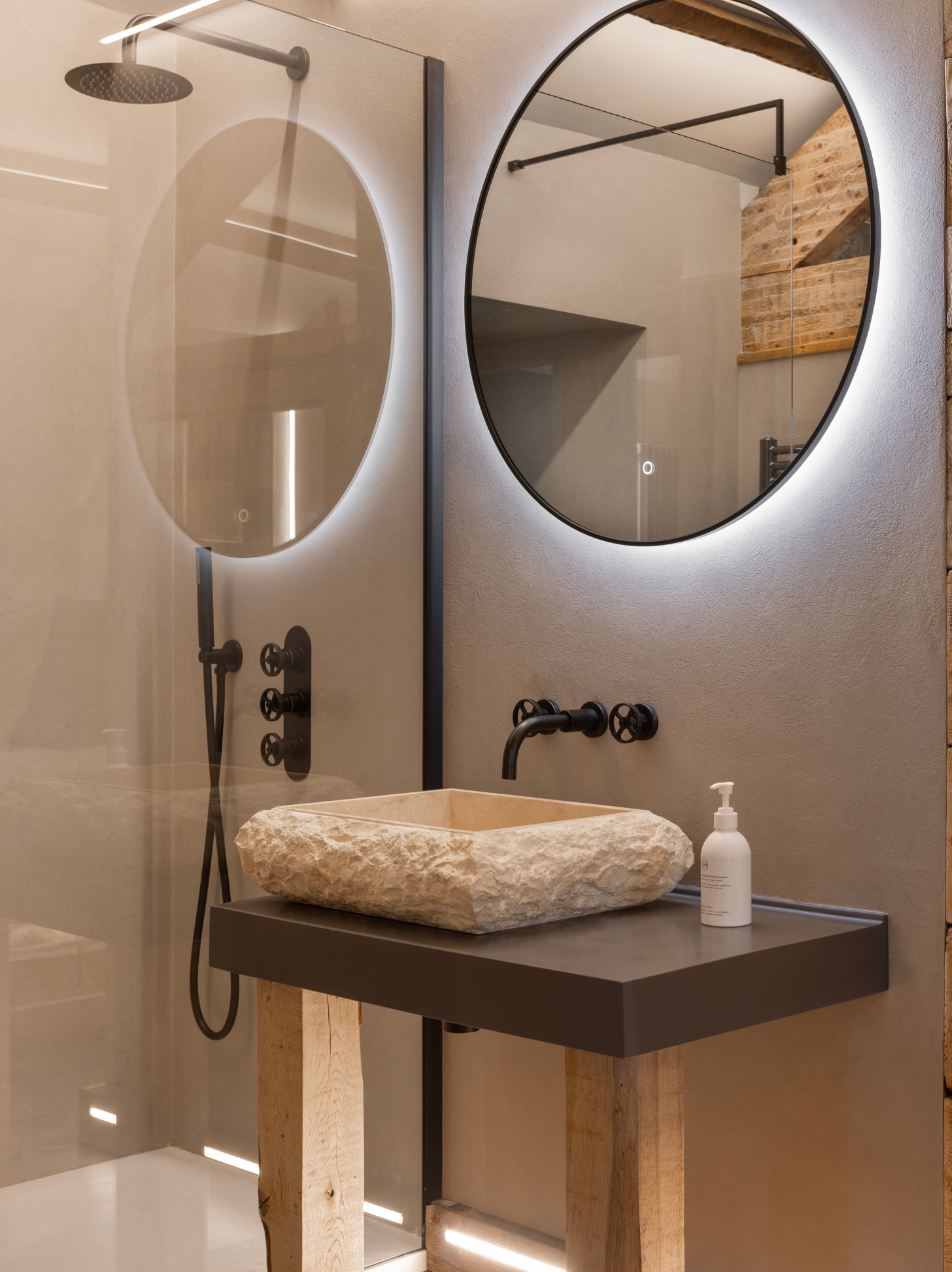 Bathroom with round mirrors, a stone sink, and a soap dispenser.
