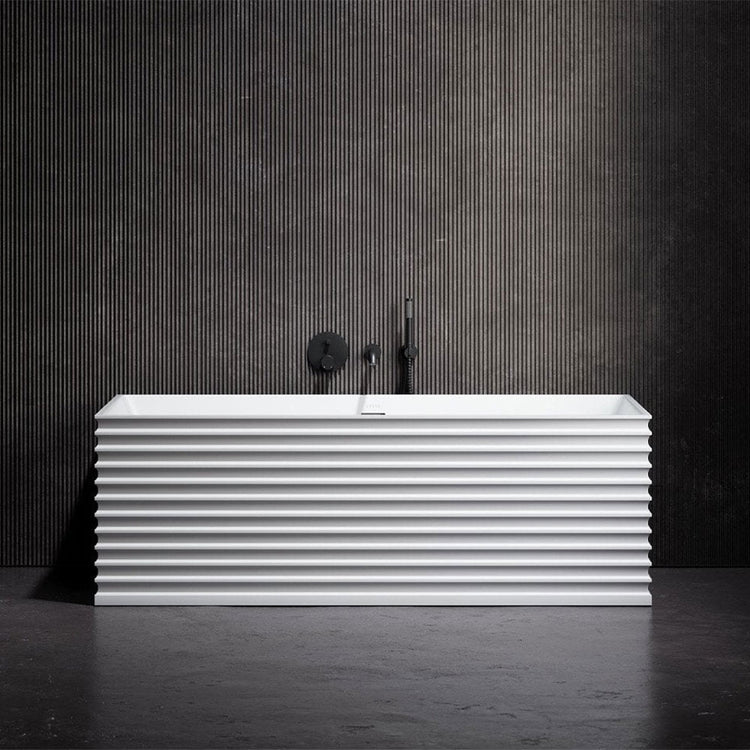 White freestanding bathtub with ribbed design against a dark striped wall.