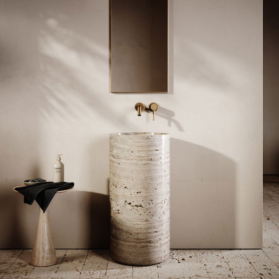 Bathroom with a stone-textured freestanding sink, gold faucet, and mirror.