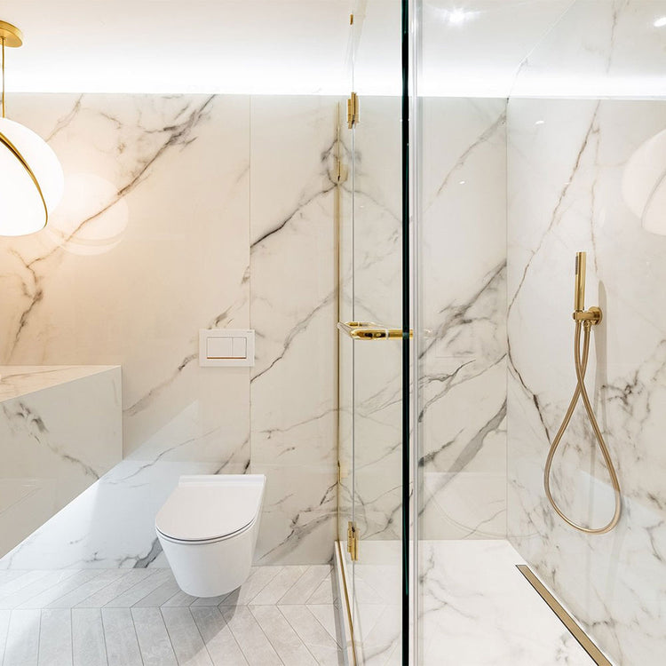 Modern bathroom with marble walls, a toilet, and a shower with gold fixtures.