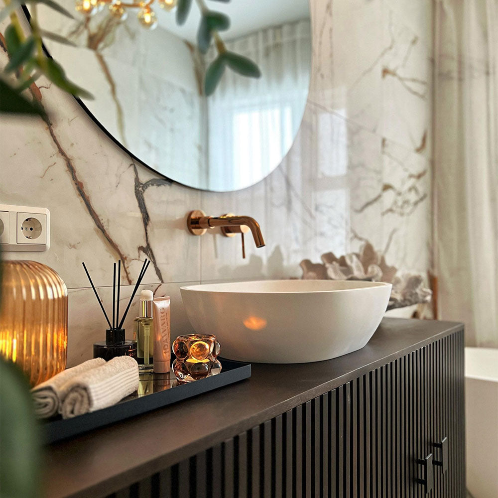 Bathroom vanity with round mirror, white sink, and decorative items.