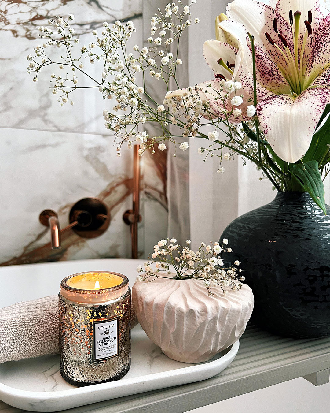 Candle, vase with flowers, and small plant on a marble surface