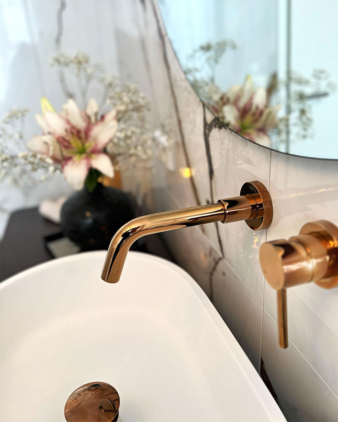 Gold faucet and handles on a bathroom sink with a mirror reflecting flowers.