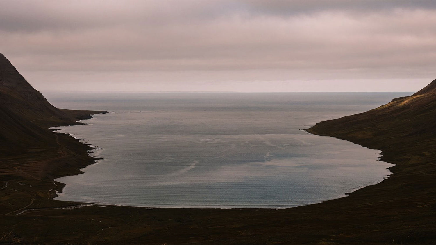 Inlet of water surrounded by mountains under a cloudy sky