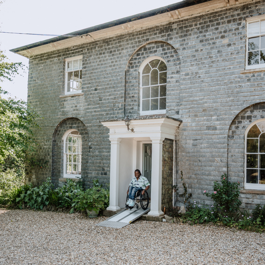 Person in a wheelchair using a ramp outside a stone building with arched windows.