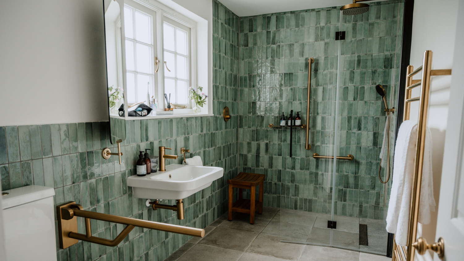 Bathroom with green tiled walls, white sink, and gold fixtures.