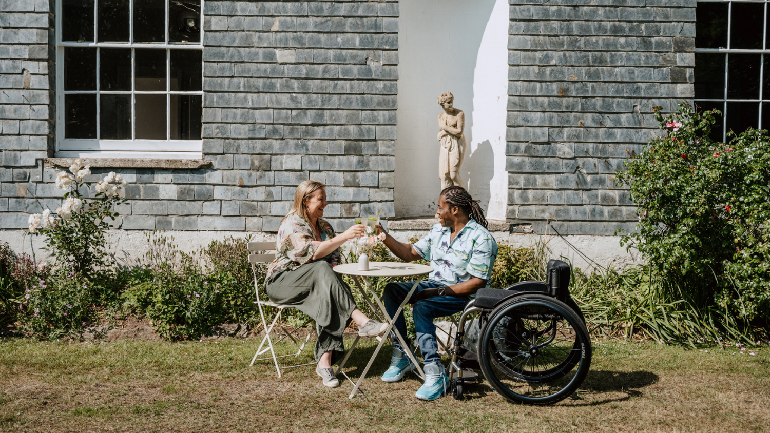 Two people sitting at a table outside a building with a statue in the background.