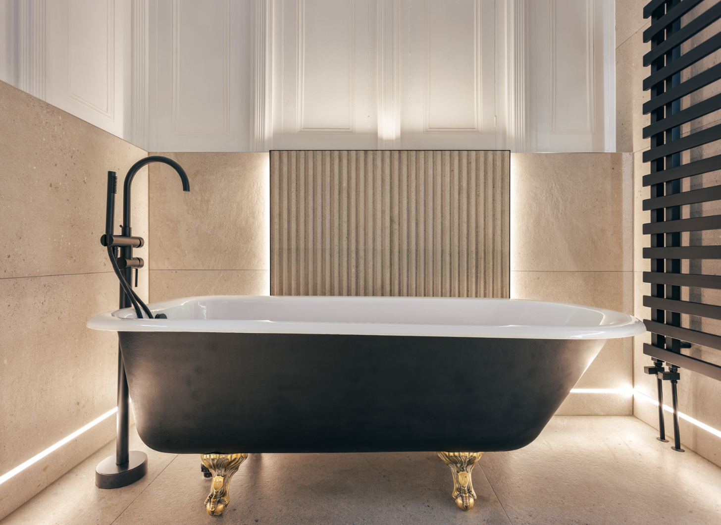 Black freestanding bathtub with gold legs in a modern bathroom setting.