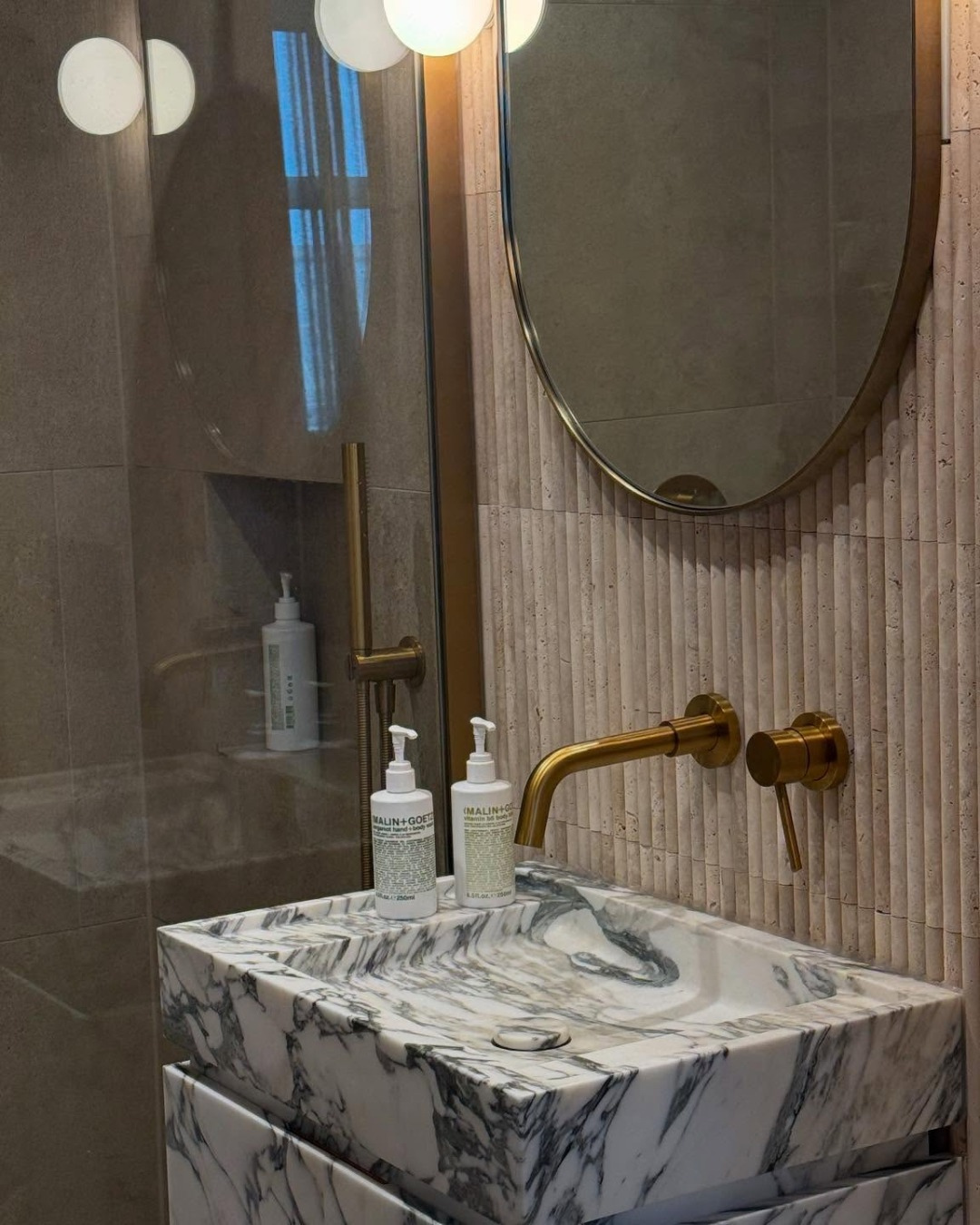 Bathroom vanity with marble countertop, gold faucet, and round mirror.