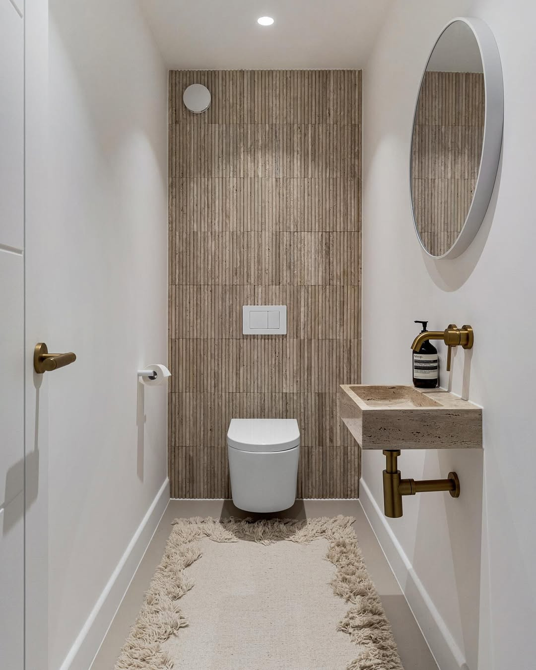 Modern bathroom with wooden tiled wall, toilet, sink, and mirror.