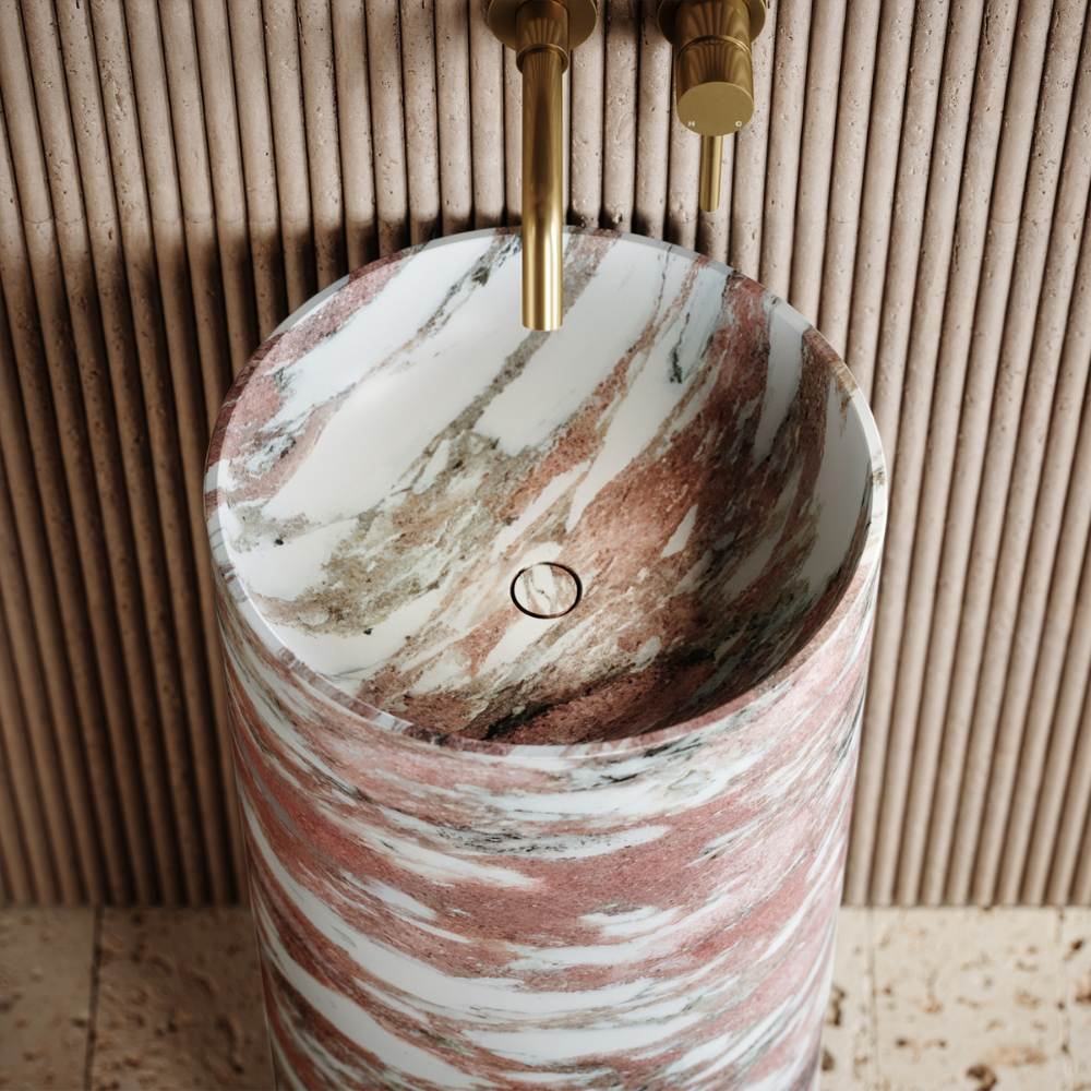Marble-patterned cylindrical sink with gold fixtures against a wooden panel background